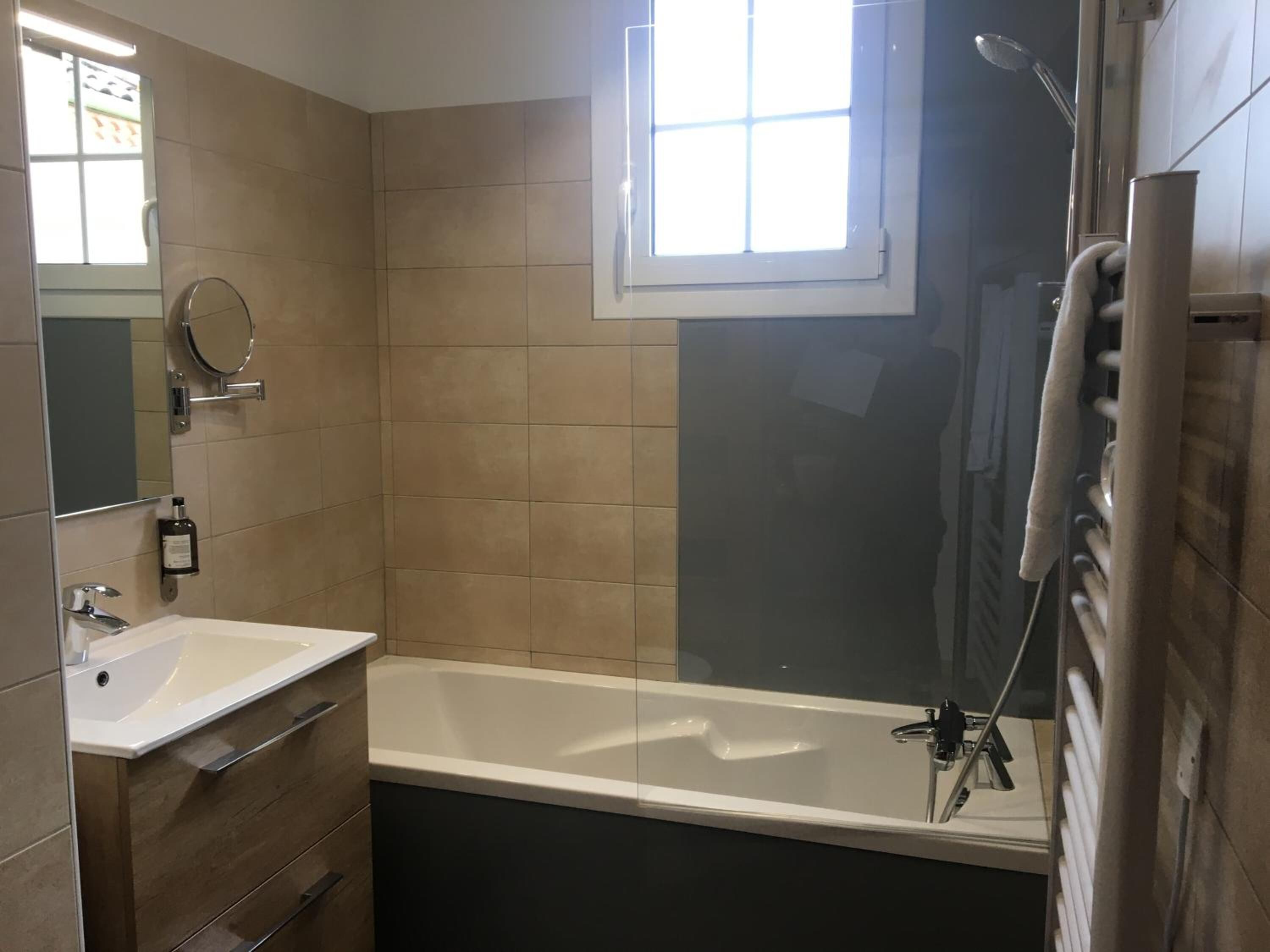 Un baño moderno con bañera, lavabo y espejo. Una ventana proporciona luz natural.