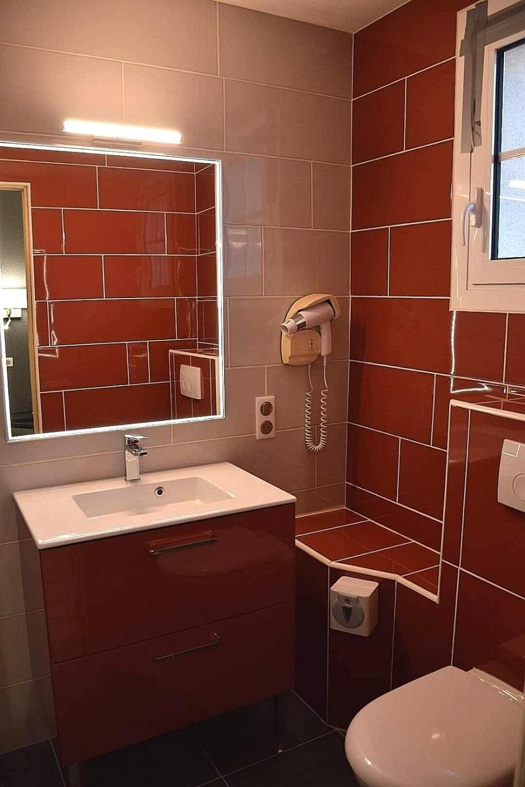 A bathroom with a sink, mirror, hairdryer, and toilet.