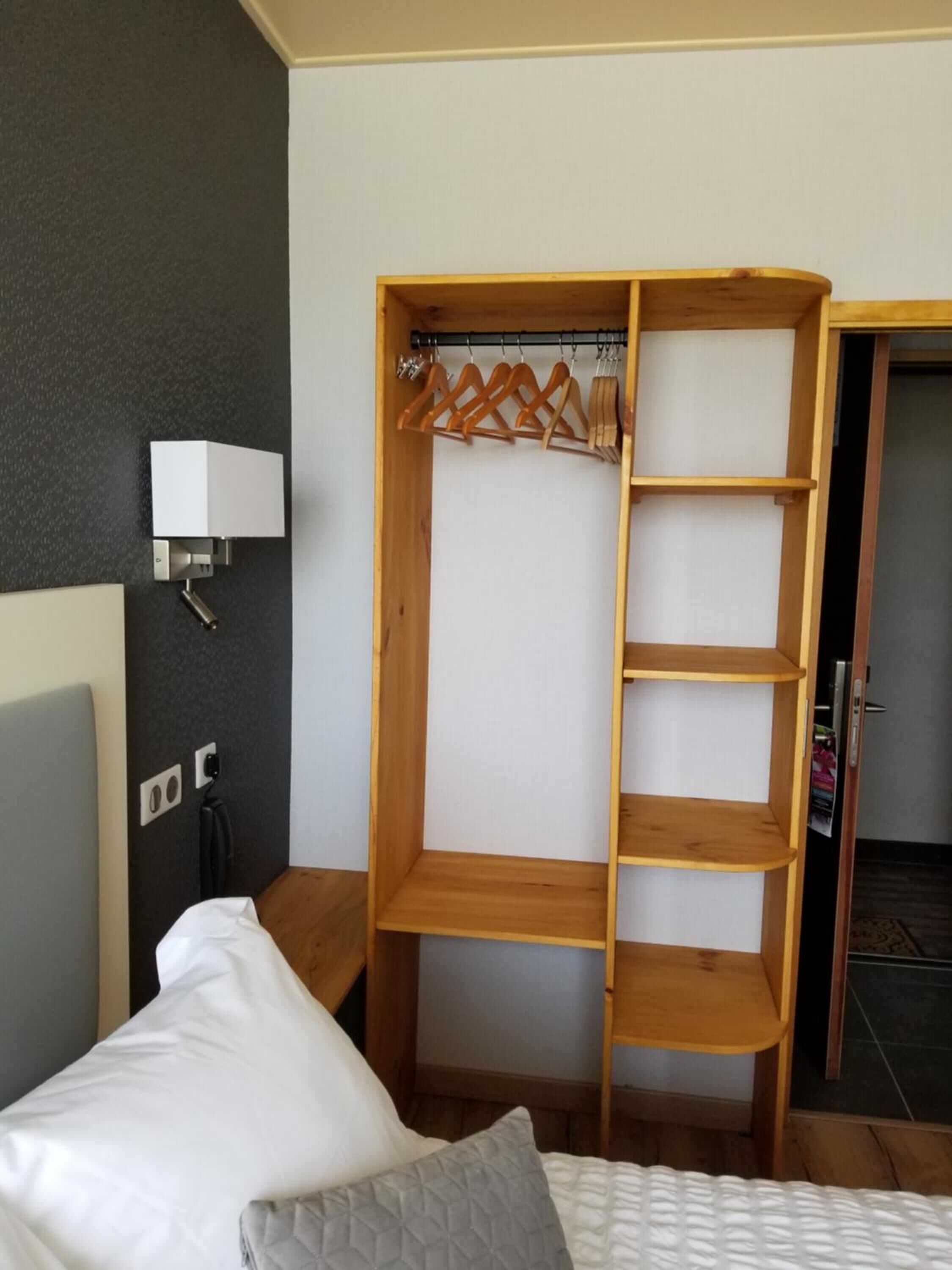 A bedroom with a wooden wardrobe, a bedside table, a lamp, and a bed.