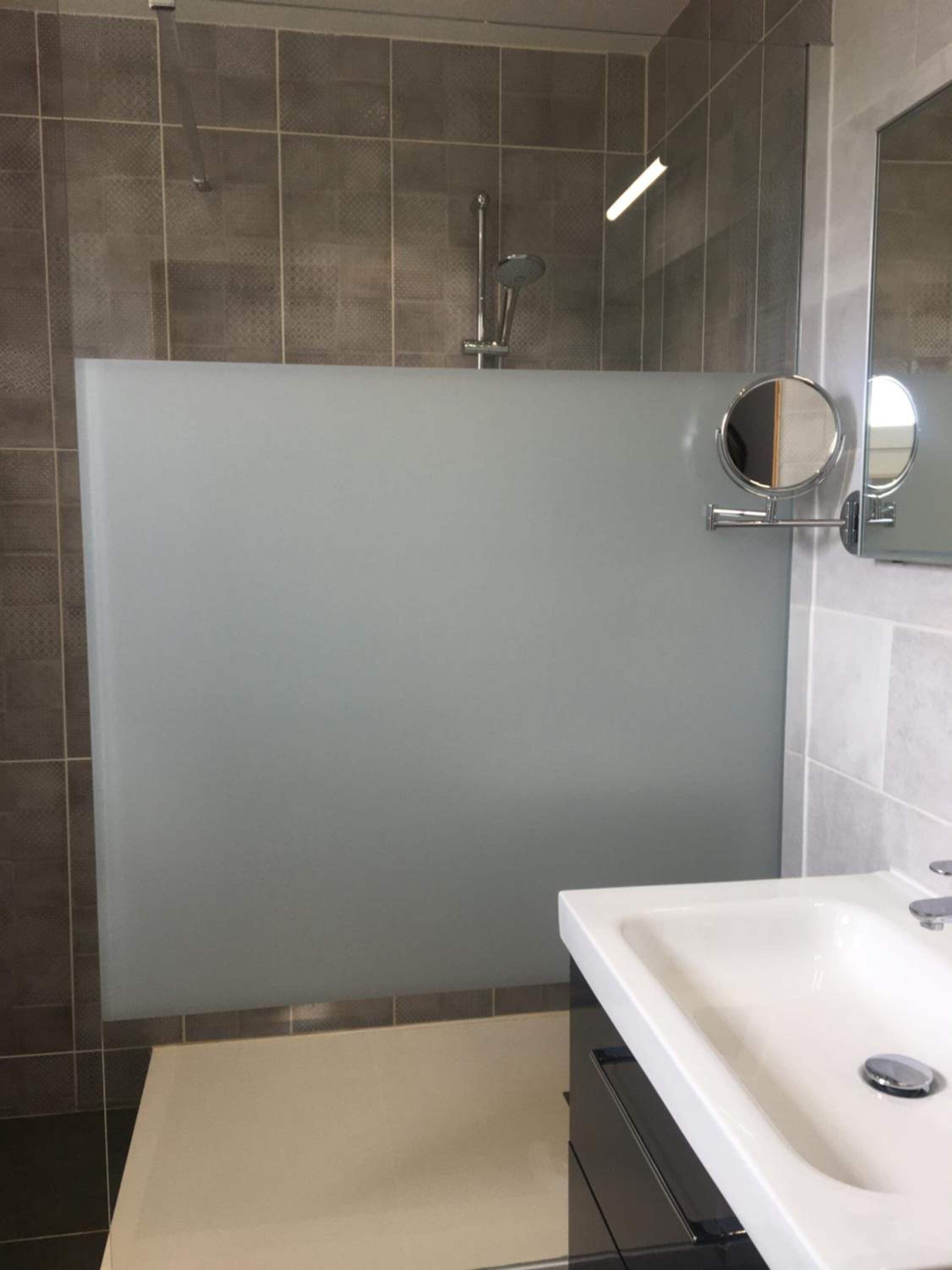A modern bathroom with a large mirror, a shower, and a sink.