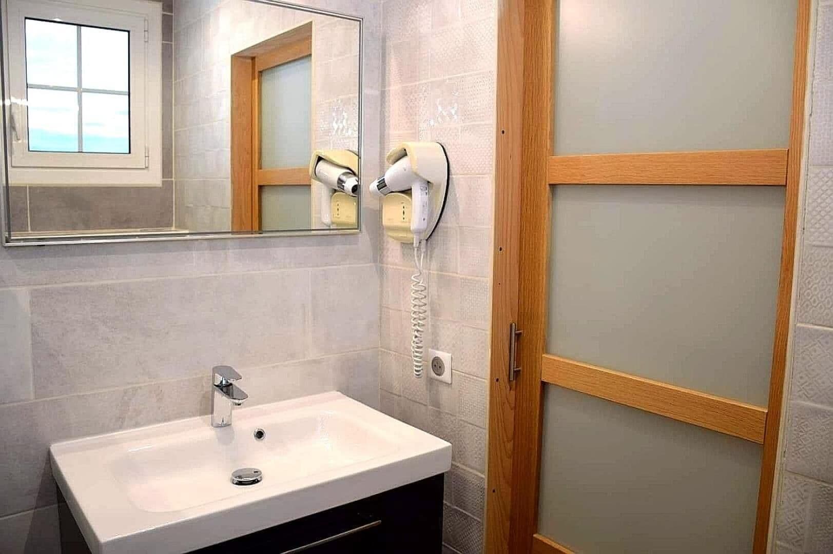 Un baño con lavamanos blanco, un espejo y un secador de pelo montado en la pared.