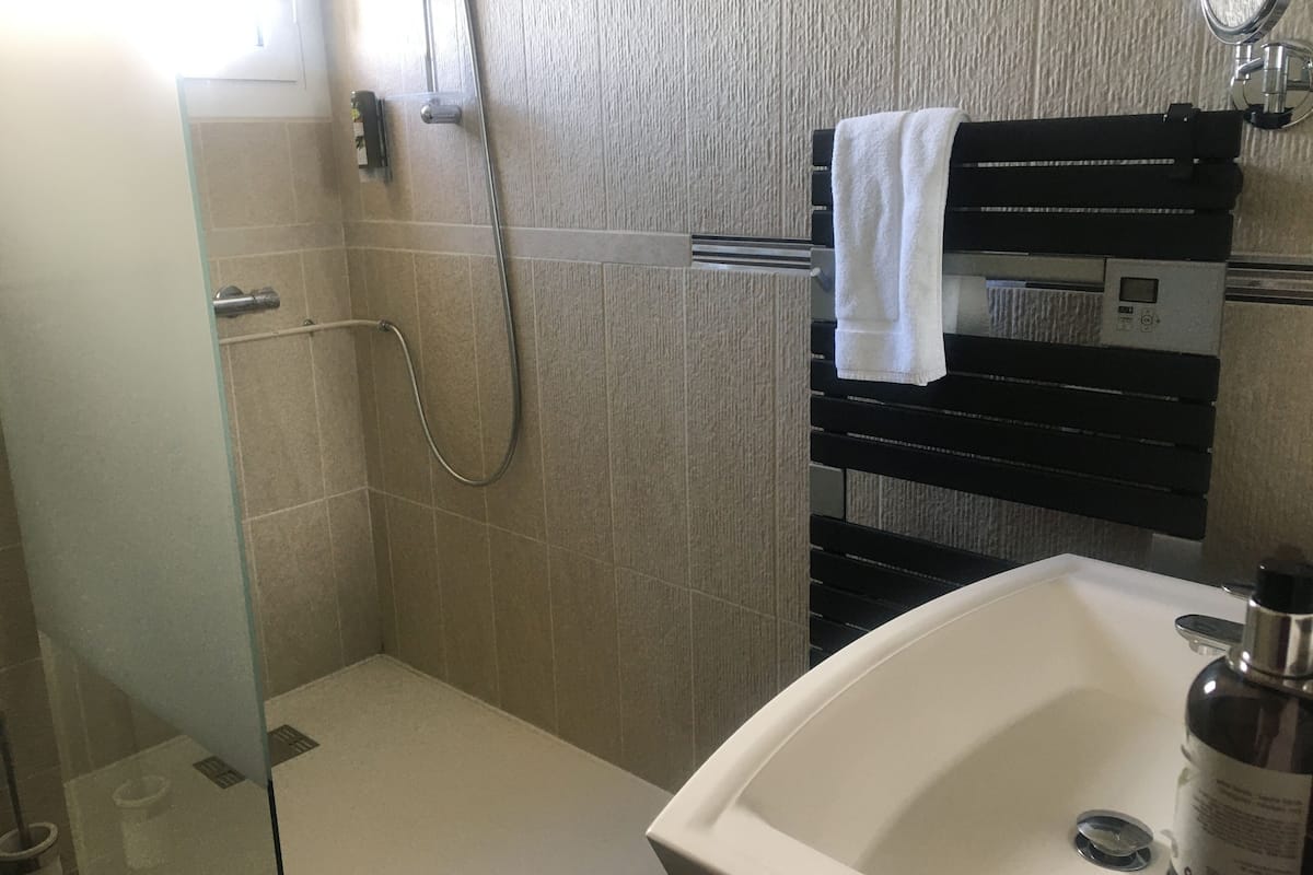 Casa de banho com cabine de chuveiro em vidro, lavatório branco e barra para toalhas.