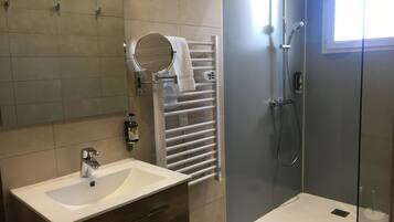 Un baño moderno con lavamanos, espejo, toallero y ducha con mampara de vidrio.