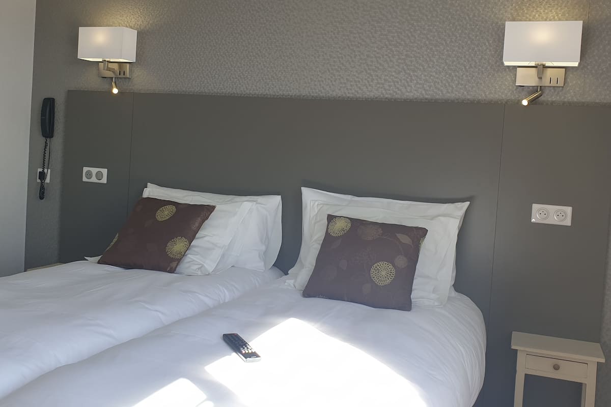 Cama bem arrumada com almofadas brancas e castanhas, mesa de cabeceira e telefone fixado na parede.