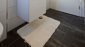 A modern bathroom with a white sink, mirror, and dark tiled floor. - Wohnung 3 (Norderney)