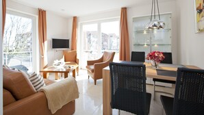 A modern living room with a sofa, chairs, a dining table, and a TV. - Wohnung 3 (Norderney)