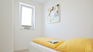 A bedroom with a bed, a window, and a wall-mounted abstract painting. - Wohnung 3 (Norderney)
