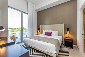 A hotel room with a large bed, a desk, and a view of a body of water through a balcony. - Bay views, luxury finishes, and coastal chic in this 1-bedroom heaven (Miami)