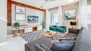Una sala de estar moderna con un sofá gris, una mesita de centro, un televisor y un sillón verde.