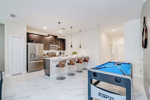 A modern kitchen with a central island, bar stools, a pool table, and a refrigerator. - 5-BR Townhouse with Pool & Theme room Near Disney (Kissimmee)