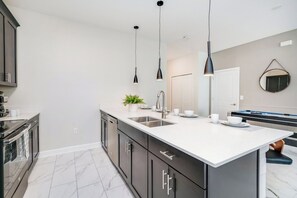 A modern kitchen with a large island, dark cabinets, white countertops, and pendant lighting.