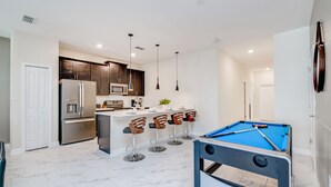 Una cocina moderna con una isla central, taburetes de bar, mesa de billar y un refrigerador.