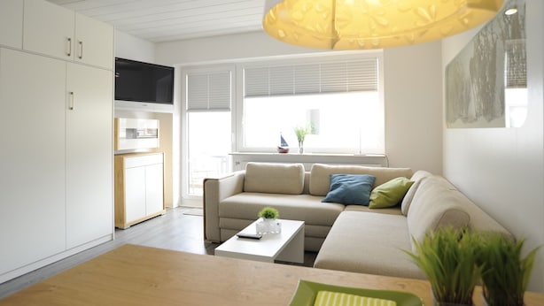 A modern living room with a sofa, coffee table, and a large window with blinds. - Wohnung Heinrichstraße 8 (Norderney)