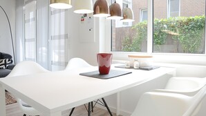 A modern dining area with a white table, white chairs, and pendant lights. - Wohnung Gartenstraße 23 (Norderney)