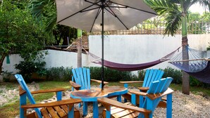 Un'area patio con un tavolo rotondo in legno, circondato da sedie blu, un'amaca e un ombrellone.