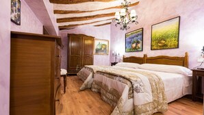 A bedroom with a wooden bed, a wooden wardrobe, a chandelier, and floral artwork on the walls. - "Casa Rural La Cuca" (Lerín)