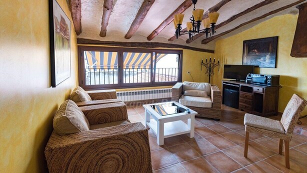 A cozy living room with a sofa, armchair, and coffee table, a kitchen area with a stove and cabinets, and large windows with striped awnings. - "Casa Rural La Cuca" (Lerín)
