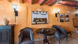 A room with rustic decor, featuring a wooden cabinet, two upholstered chairs, a round table with decorative items, and wall-mounted light fixtures. - "Casa Rural La Cuca" (Lerín)