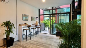 Um interior moderno com piso de madeira, área de bar com banquetas e grandes janelas com vista para o exterior.