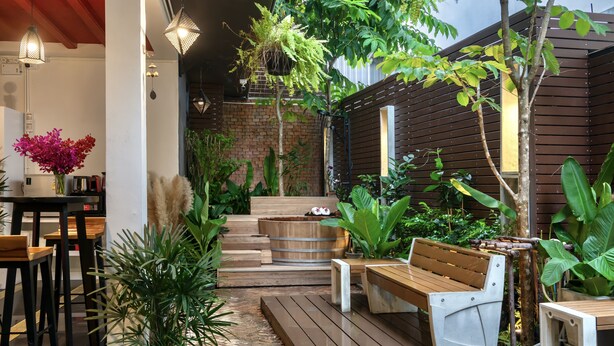 Um deck de madeira com área de estar ao ar livre, um vaso de madeira e diversas plantas.
