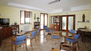 Una habitación amplia con una gran mesa de madera, varias sillas azules, un televisor, una estantería y una estatua.