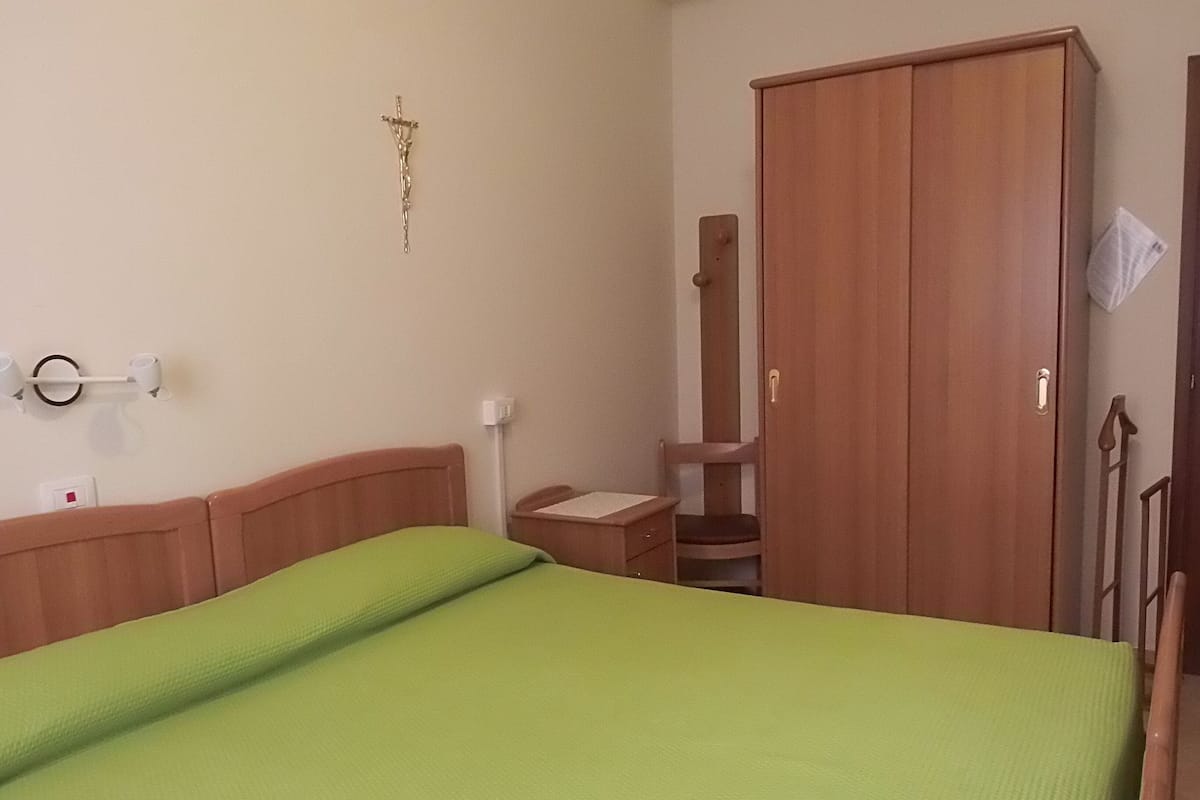 Een slaapkamer met een bed, een houten garderobe, een stoel en een wandlamp.