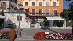 Un edificio de dos pisos con fachada de piedra, balcones con jardineras y una calle adoquinada.