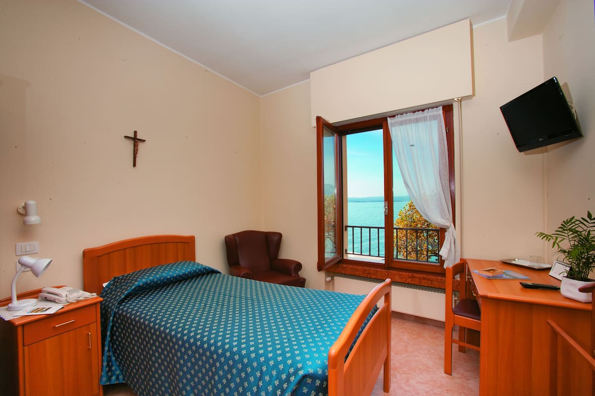 Een slaapkamer met een bed, een bureau, een stoel, een televisie en een raam met uitzicht.