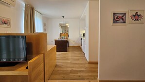 En modern lägenhet med trägolv, en TV placerad på ett träbord, ett kök med matplats och konstverk på väggarna.