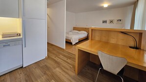 Ett litet rum med ett pentry, en säng, ett skrivbord och en stol.
