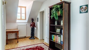 Ein Zimmer mit Holzboden, einem roten Teppich mit Muster, einem Bücherregal voller Bücher, einer Topfpflanze und einer Statue.