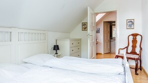 Ein Schlafzimmer mit einem Bett, einem Schminktisch, einem Stuhl und einer Tür zu einem anderen Raum.