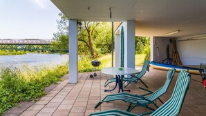 Eine überdachte Terrasse mit Tisch, Stühlen, einem Grill und einem Kanu.