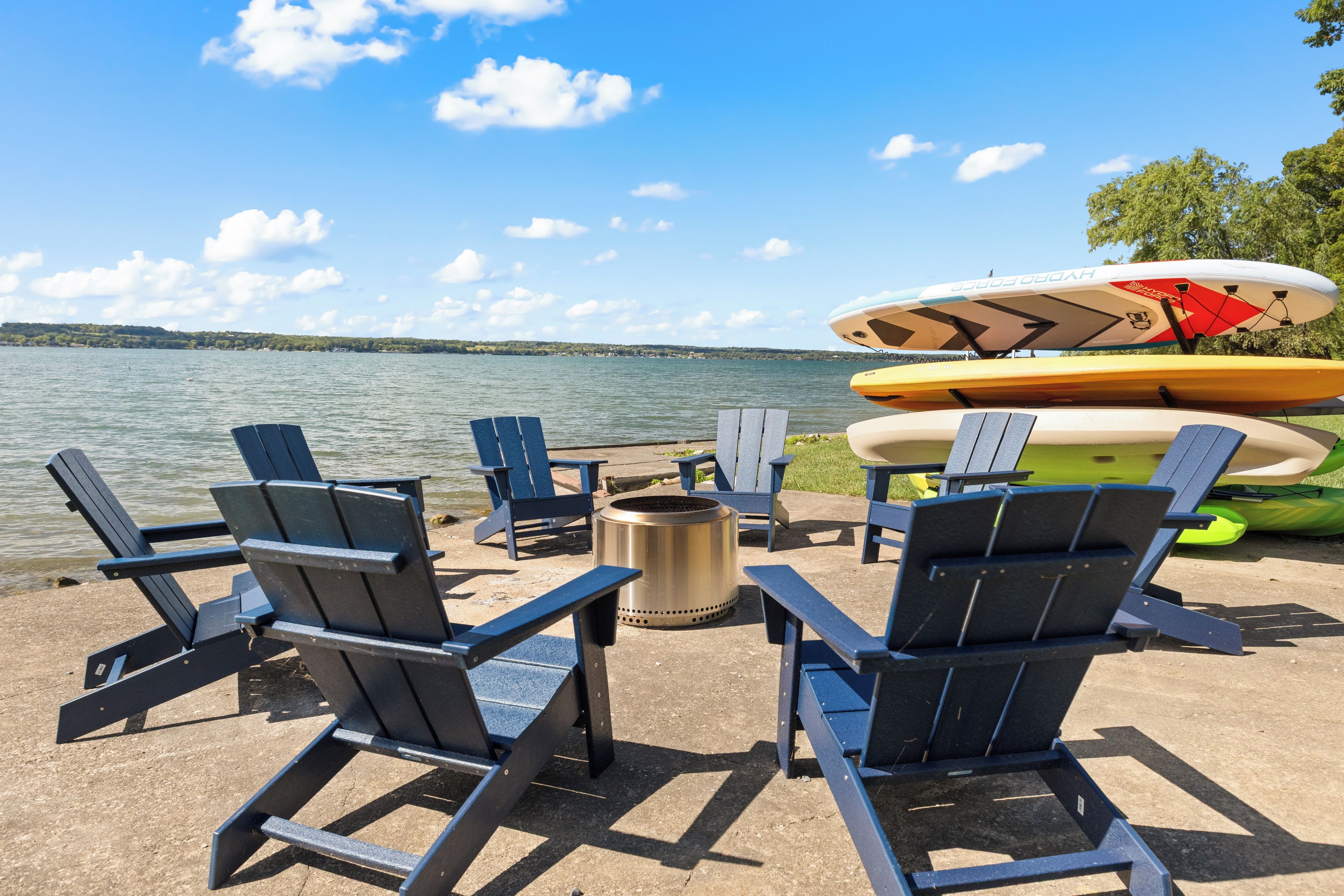A lakeside seating area with Adirondack chairs, a fire pit, and kayaks.