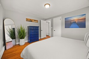 A bedroom with a large bed, a dresser, a mirror, a potted plant, a door, and a wall-mounted picture. - Wide Open Views: lakefront home with hot tub (Geneva)