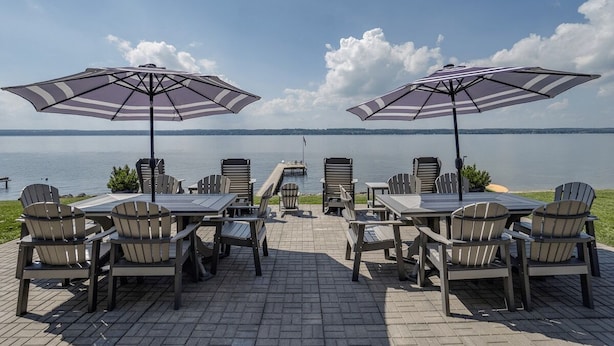 Un patio con sillas Adirondack y mesas, dos grandes sombrillas a rayas, y vista a un lago.