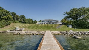 Una casa con un muelle que da a una masa de agua cristalina, rodeada de vegetación y un césped bien cuidado.