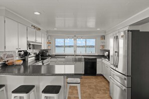 A modern kitchen with a view of the water, stainless steel appliances, and a bar area with stools.