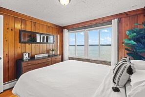 A bedroom with a large bed, wooden walls, a window with a view of a lake, and a sign reading 'SENECA LAKE'.