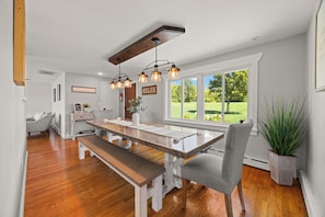 Un comedor espacioso con una mesa y banco de madera, ventanas amplias que dan a un paisaje verde, y un techo con vigas a la vista e iluminación colgante.