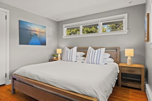 Un dormitorio con cama, mesitas de noche, una ventana y un cuadro en la pared.