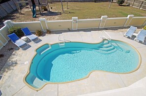 A rectangular swimming pool with a diving board, surrounded by a beige wall and a small garden area with a swing set. - SS93- Semi-Oceanfront Home with 7 BRs and beautiful ocean views! (Kitty Hawk)