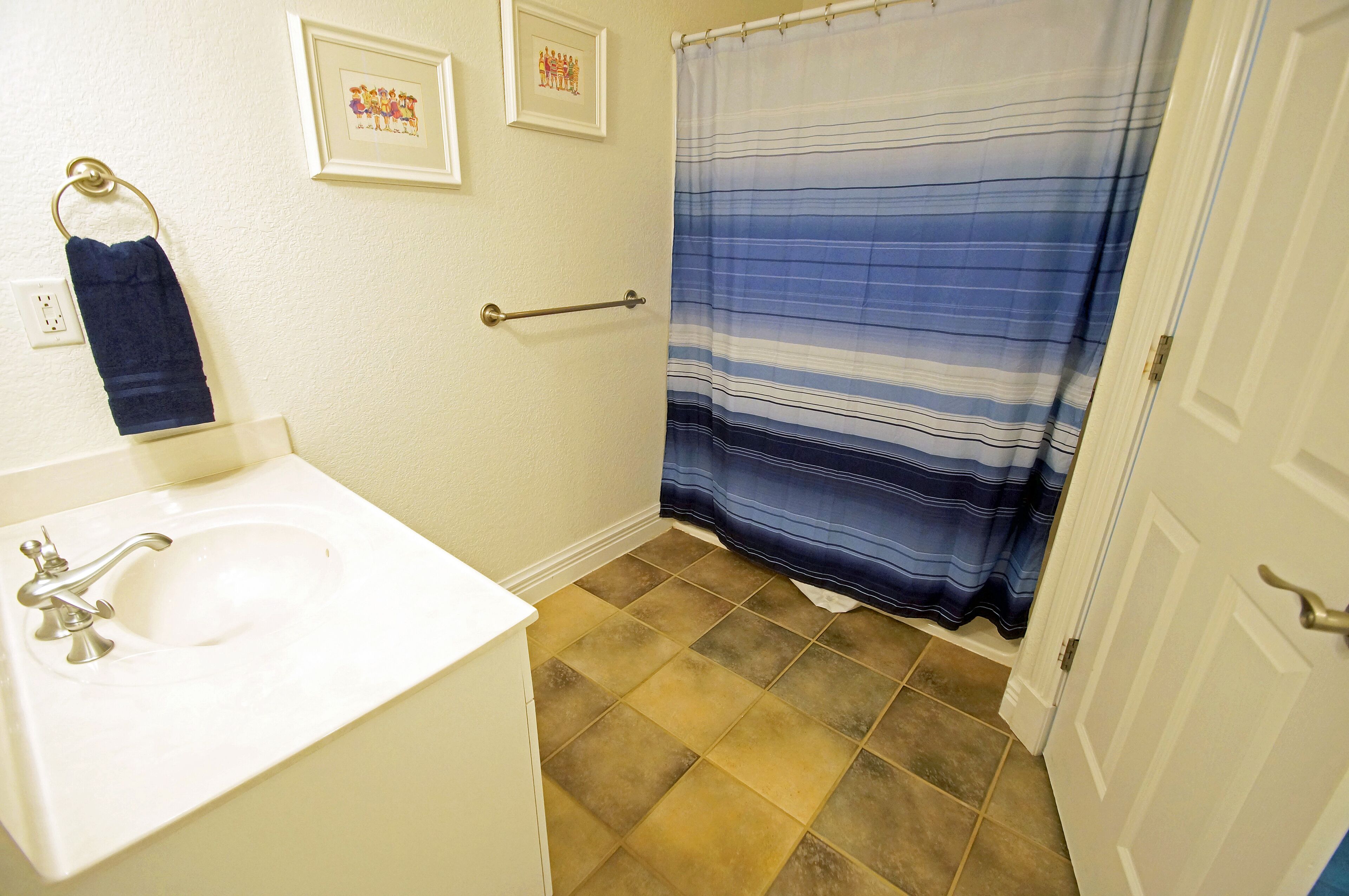 A bathroom with a white sink, a towel rack, a framed picture, a striped shower curtain, and a door.