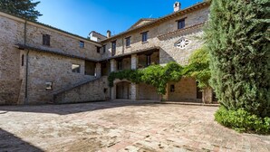 A courtyard with stone buildings, a staircase, and a large tree. - Borgo Colle Ridente 13, Emma Villas (Camerino)