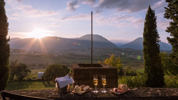 A scenic view with mountains, a wooden table with food and drinks, and a clear sky. - Borgo Colle Ridente 13, Emma Villas (Camerino)