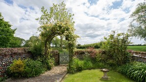 Un jardin avec un chemin en pierre, une porte en bois et un abreuvoir à oiseaux en pierre.