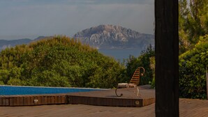 Terraza de madera con piscina y una silla con vista a un paisaje montañoso.