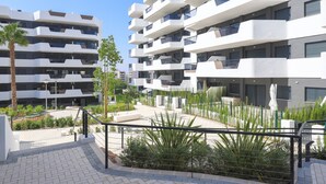 A modern multi-story residential building with balconies, a landscaped courtyard, and a clear sky. - Myflats Luxury Arenales (Elche)