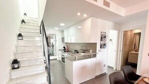 A modern kitchen with white cabinets, a central island, and a dining area with a table set for two. - Myflats Luxury Arenales (Elche)