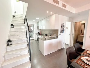 A modern kitchen with white cabinets, a central island, and a dining area with a table set for two. - Myflats Luxury Arenales (Elche)
